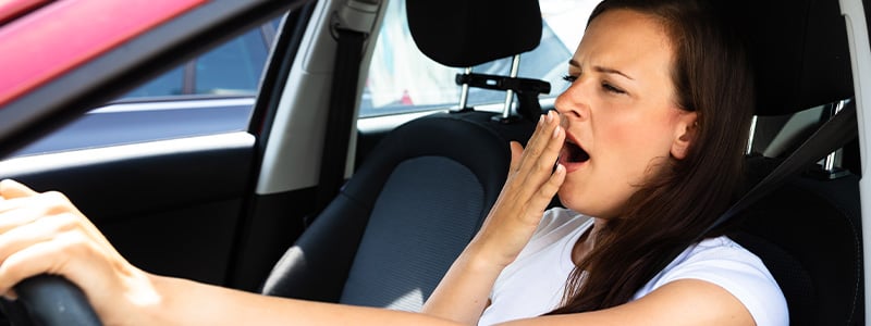 Woman in car yawning.