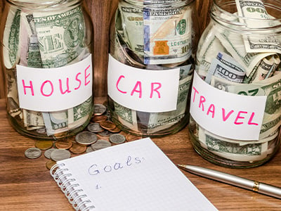 Financial goals with jars of money for house, car, and travel