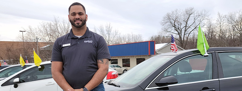 Aaron Valdez, General Manager at America’s Car-Mart of Saint Joseph, MO, standing on his lot