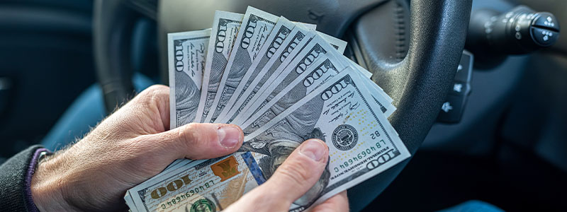 Man holding several $100 bills while sitting in a car