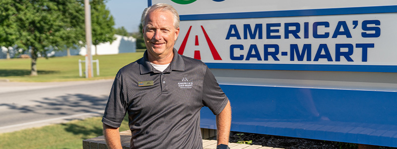 Mike Ward, Car-Mart's Vice President of Associate Support, standing by the America's Car-Mart sign outside of the corporate office in Rogers, Ark.