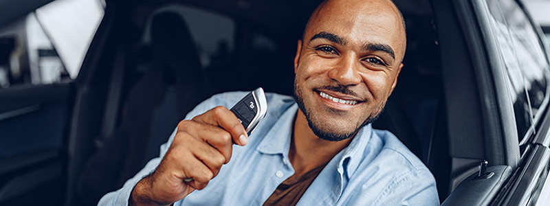Man in blue shirt sitting in driver's seat of car holding car keys and smiling