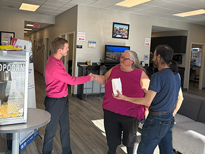 America's Car-Mart Customers, Jana and Anthony Degadoi shaking hands and eating popcorn at Springfield South, Missouri Car-Mart.